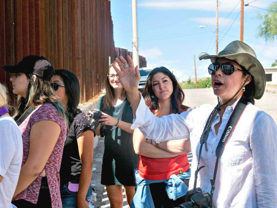 woman talking to a group of people standing at the border wall in southern Arizona