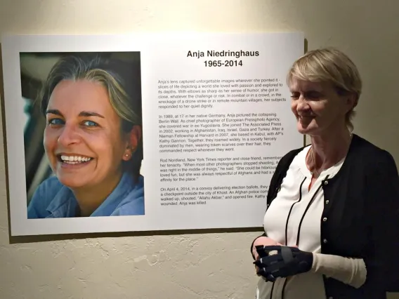 woman standing next to a sign at the entrance of a photo gallery; sign has an image of the female photographer and a description of the show