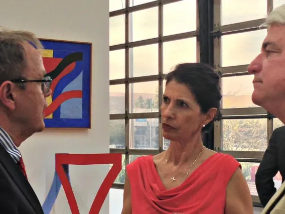 woman in red dress speaking with two men indoors