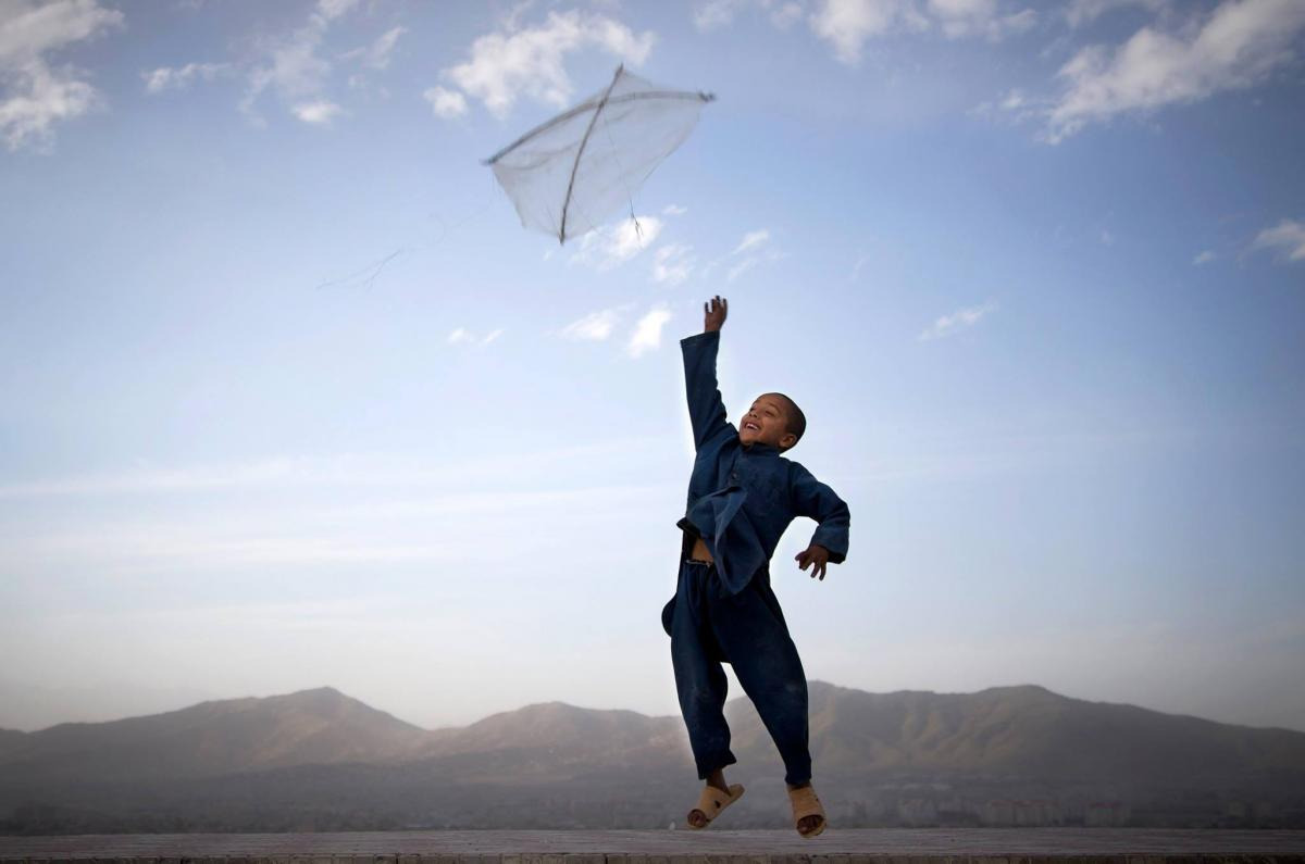 boy jumping while reaching to touch a kite