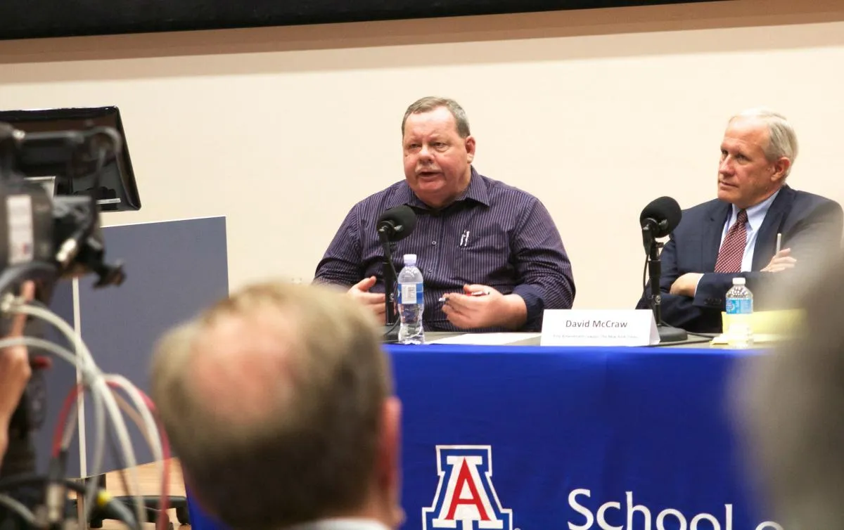 man sitting at a table speaking to a crowd