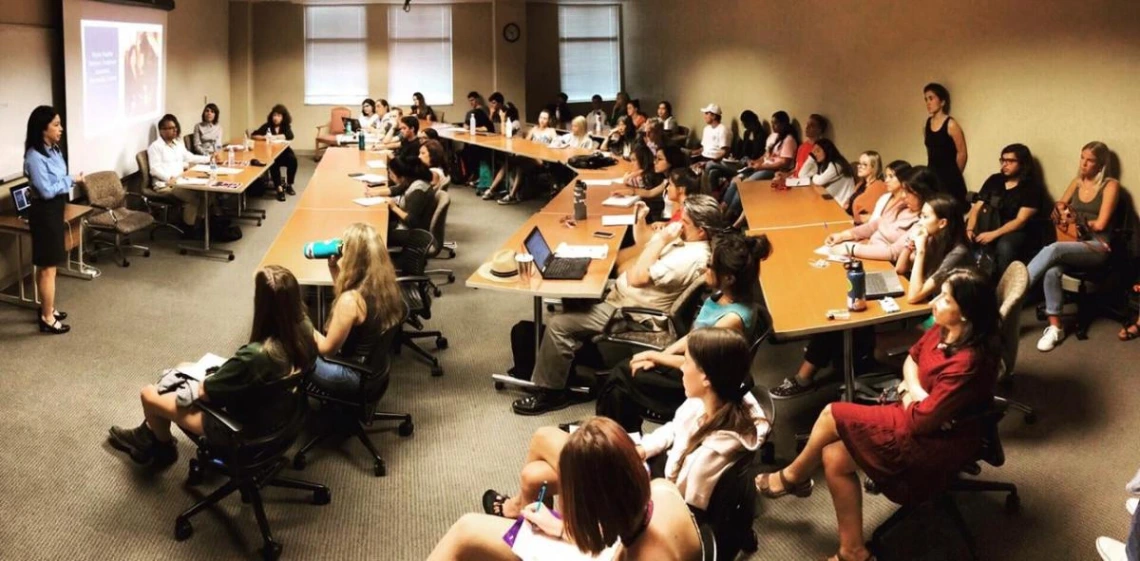 classroom filled with students, professor at the front speaking